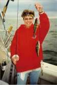 Woman standing on boat holds up a triple of perch on her line.