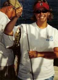 Smiling woman holds up two perch on her fishing line.