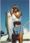 Woman strains to hold up a trophy steelhead with both hands.